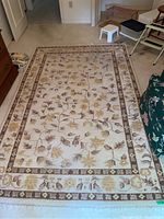 Full view of the rectangular patterned rug on a carpeted floor, showing wear and discoloration.