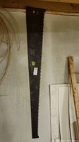 Full length view of the vintage oversized saw cutting edge hanging vertically against a wall showing its entire length of 69 inches and large cutting teeth.