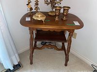 Front and top view of the wooden side table with various decorative metal items on top. Shows the tabletop shape, turned legs, and scalloped apron detail.