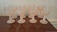 Eight pink frosted glasses with floral and grape motifs, each standing about 5 inches tall.