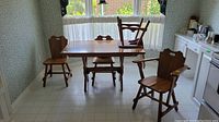 Full view of dining table with three dining chairs around and captain's chair pulled out