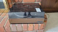 Turntable with closed dust cover showing scratches and smudges on the cover and power cord at the back