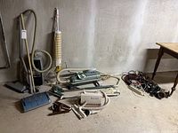Overview photo of all vacuums, hoses, cords, and light fixtures laid out on a floor against a wall.