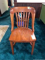 Full front view of a wooden chair on blue carpet showing slatted back and smooth seat.