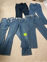 Five pairs of women's jeans laid out on a carpet, varying shades of blue, with tags attached.