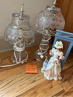 Pair of vintage glass lamps and Victorian style porcelain doll with blue frame on hardwood floor