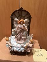 Lighted cherub figurine with two musical angels on cloud base with decorative arched window background.