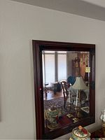 Full view of the mirror hung on a wall, showing its rectangular shape, dark wood frame with decorative carved edges, and the reflection of a room with furniture.