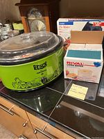 Green Nesco Potluck crock pot with glass lid, Rival Little Dipper fondue set unopened in box, mini pie maker box visible behind them.