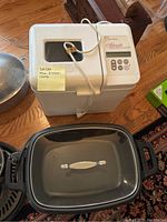 Cuisinart bread maker and slow cooker visible on hardwood floor alongside a black cooking pot