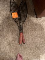 Two metal grill baskets with wooden handles on carpet