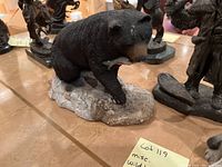 Photo of black bear statue holding a fish on a rock base, showing detailed fur texture and paint.