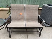 Two-seat outdoor glider bench with bronze metal frame and taupe sling fabric seating