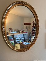 Front view of the oval mirror showing the gold decorative frame and reflection of room interior.