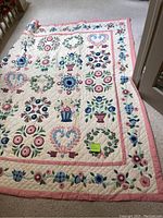 Photo of a handmade floral patterned quilt laid out on the floor, showing full view and design details with a measuring sticky note indicating size.