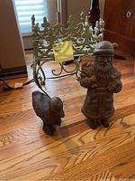 Three items on wooden floor: a rustic Santa figurine, a duck figurine, and an ornate green metal plant holder.