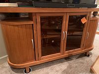 Front view of the wood TV stand showing two glass center doors, curved side cabinets, and silver handles.