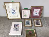 Photo showing all seven art pieces together including framed painting, watercolour, botanical and sea-themed prints on a carpeted floor against a wall.