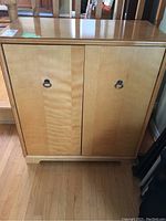 Front view of the wood cabinet showing two doors with metal ring pulls and smooth light wood finish.
