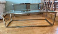 Front and side view of the coffee table showing metal frame and glass top on hardwood floor