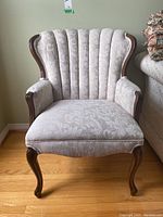 Front view of the ivory damask upholstered armchair highlighting the scalloped back and carved wood arms and legs.