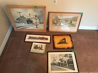 Six railway art pieces arranged on carpet: two large framed prints, two small framed engine prints, one wooden engine plaque, and one large black and white framed photo.
