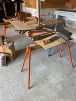 Photo showing pair of orange metal sawhorses with two pieces of plywood laid across for a work surface. Various woodworking hand tools visible on top.