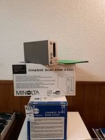 Two Konica Minolta DiMAGE Scan Elite 5400 units: one scanner on its box and another unopened box with a green folder nearby