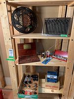 Shelf with round cast iron wood stove lid, farmhouse vent cover, vintage tap & die set, wrench set, battery charger box and furniture casters.