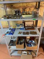 Full view of metal shelving with multiple shelves containing jars of screws, assortments of hinges, knobs, packaged riveting tools, and cardboard boxes with more hardware.
