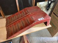 Side view of a single red plastic wheel ramp showing length and angled incline with ridges for tire traction, with visible dirt and wear marks.