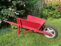 Side view of the red painted wooden wheelbarrow with single rubber tire on metal rim, showing handles and tray.