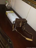 Overall view of the lot showing the brown leather binocular case with straps and the IQ Panel 2+ alarm box on a dark wood surface.