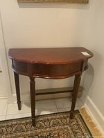 Front view of demi lune shaped wood table with curved apron and decorative legs