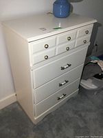 Front view of white dresser with four drawers and brass/ceramic handles, blue ceramic lamp on top.