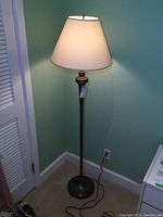 Full view of 62-inch floor lamp with beige fabric shade, located next to wall outlet and door.