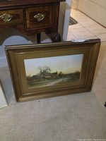 Framed signed print showing a rural landscape with a cottage, frame gold-tone and showing wear.