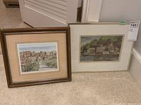 Two framed prints leaning on carpeted floor: left is a larger Robin Hoods Bay print, right is a Glenora Ferry print with white matting.