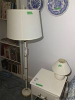Floor lamp standing next to bookshelf, ivory and brass base with white shade