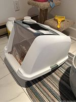 Side view of the Cat It litter box, white plastic structure with translucent flap door at front, pellet-style litter inside.