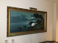 Full view of the large oil painting hanging on a wall, showing the gold frame and attached light.