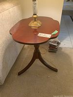 Three-legged wooden side table next to couch with shaped oval top and warm brown finish, showing general view