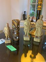 Four vintage carved figures including three human figures and one abstract figure on a reflective black surface.