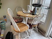 Full view of round drop leaf table with four chairs around it, table has some kitchen items on it though not included in sale