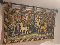 Full view of the tapestry hanging on a rod showcasing the unicorn and lion with heraldic shields and leafy border.