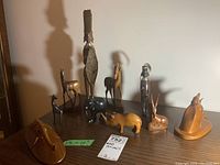 Overall group of nine vintage African wood carvings including animals and human figures in natural wood tones, some showing repaired elephant trunks and varying sizes from 2.5 to 14 inches tall
