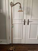 Full view of the antique standing lamp showing the tall cast iron base and the frosted glass shade with fluted edge suspended from an ornate curved arm.