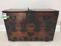 Front-facing view of chest showing drop-down front panel, central lock plate, D-ring handles and decorative iron hardware across surface