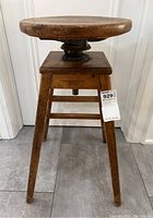 Front view of the antique wooden industrial stool, showing round wooden seat and four wooden legs with three horizontal rungs on one side, two missing on the other side.