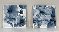 Front view of two square blue and white floral paintings side by side on a shelf.